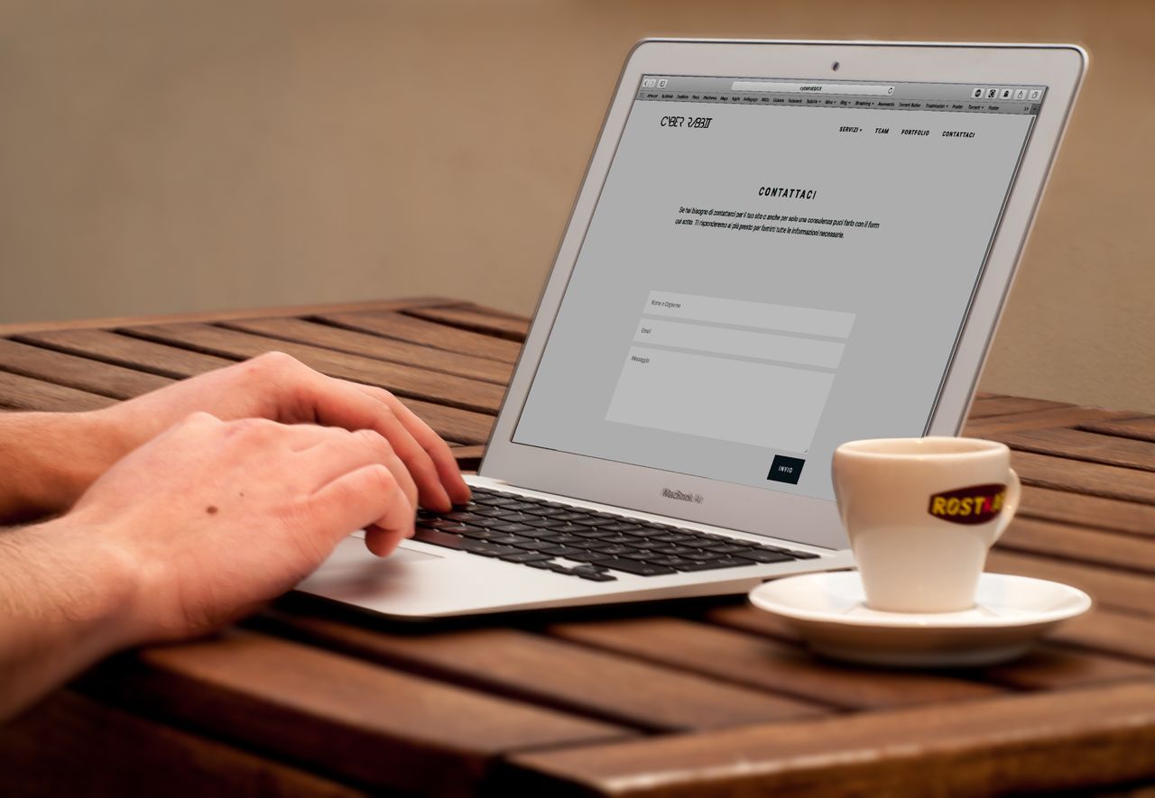 creative Close-up of hands typing on a laptop next to a cup of coffee on a wooden desk.